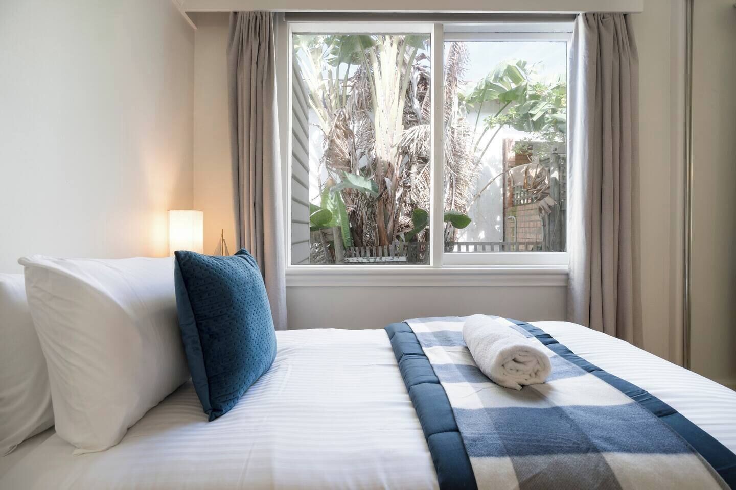 Habitación de hotel con cama, ventana con cortinas y vistas a zonas verdes.