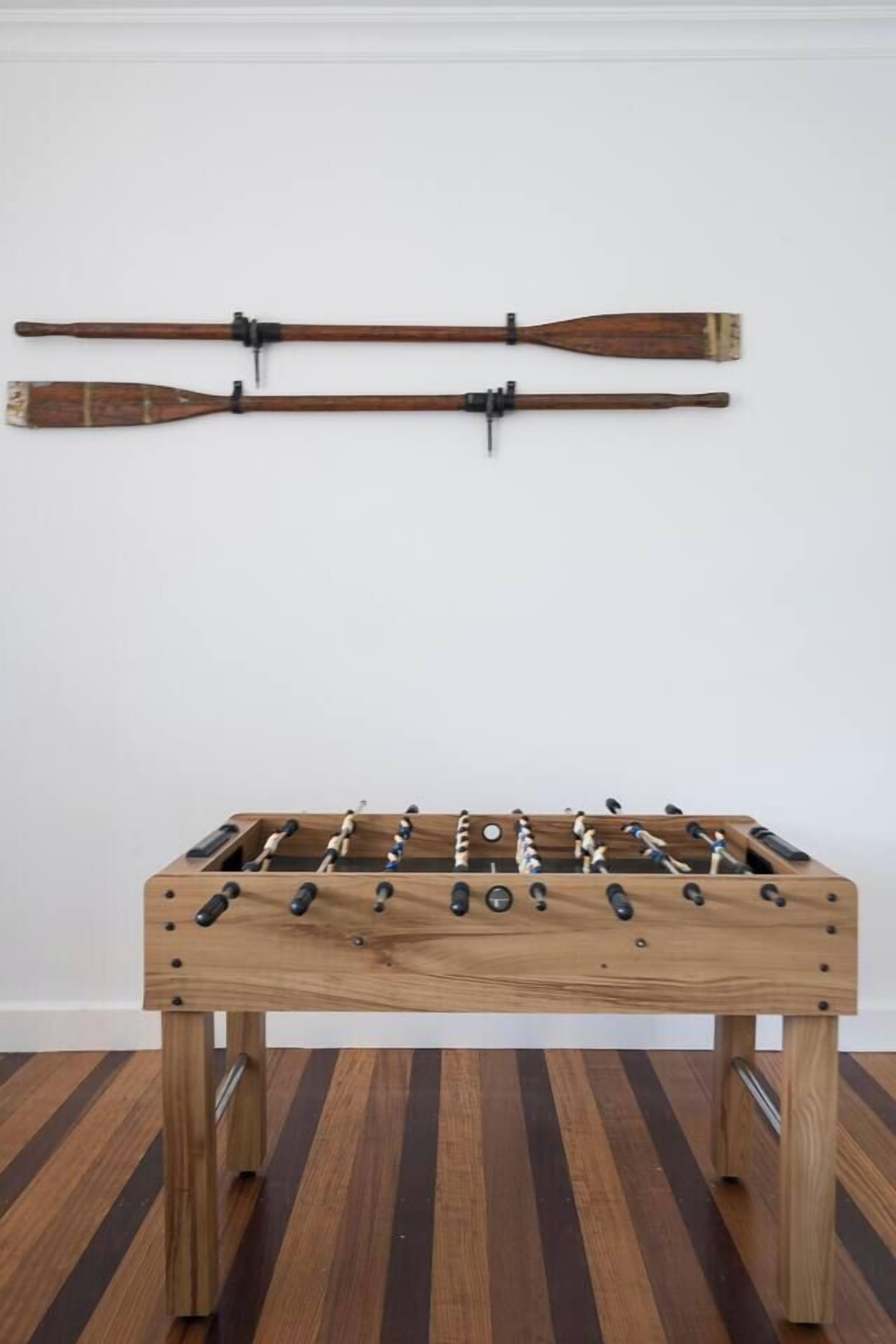 A wooden foosball table with a classic design, positioned against a plain wall.