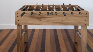 Een houten tafelvoetbalspel met een klassiek ontwerp, geplaatst tegen een effen muur.