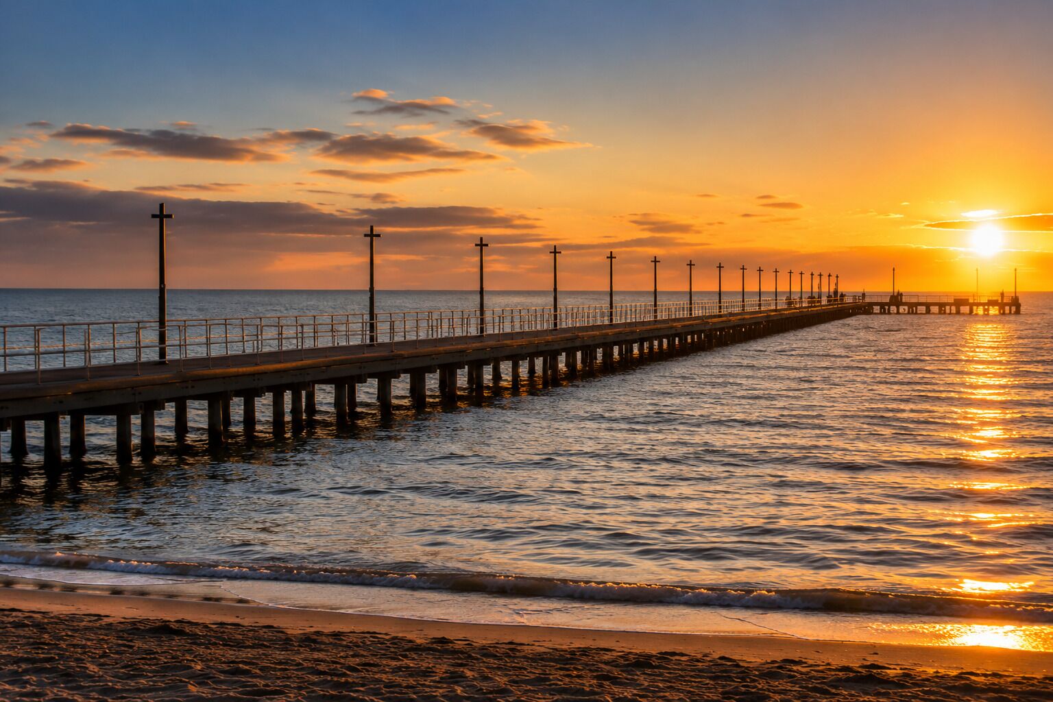 A pier extending into the sea with a sunset in the background.
