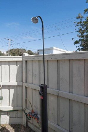 A metal showerhead attached to a vertical pole, with a white wooden fence in the background. - Willow Landing Beach House with Private Jetty (Frankston)