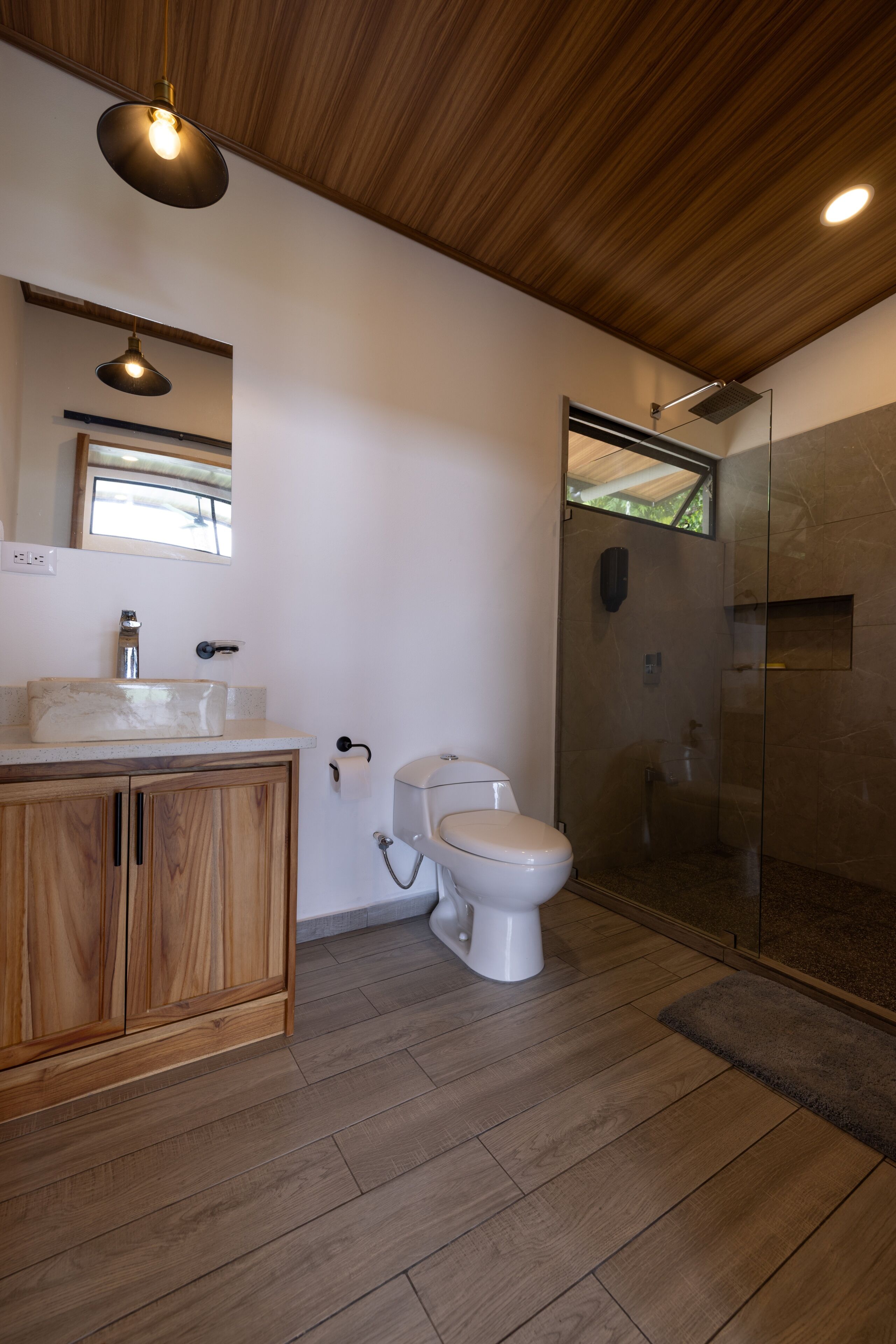 A modern bathroom with a wooden vanity, a toilet, and a glass-enclosed shower.