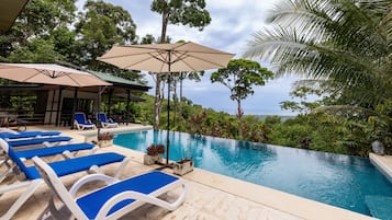 A pool area with lounge chairs, umbrellas, and a view of the ocean.
