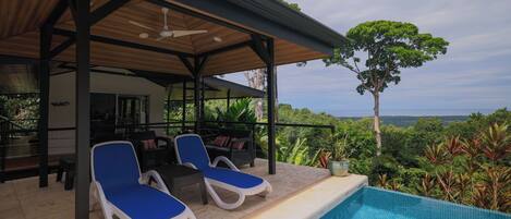 Un espacio exterior techado con piscina, sillas de descanso y vistas del paisaje.