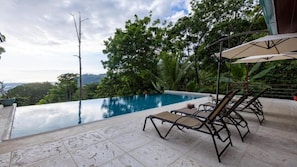 An infinity pool with lounge chairs and umbrellas, surrounded by lush greenery and a view of the landscape. - Casa Odi-Sea 2.0 (Savegre)