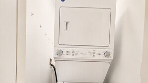 A white washing machine in a narrow hallway with a blue detergent container nearby.