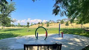 A park bench, a circular playground structure, and a fenced area with houses in the background.