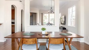 A dining area with a wooden table, two chairs, a potted plant, and a view of the kitchen through an archway. - home away from home spacious 3b 2b mobile home covered back porch with hot tub.. (seven points)