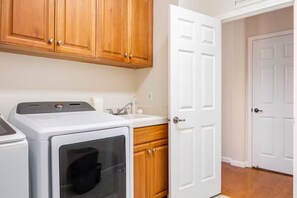 A laundry area with a washing machine, a dryer, wooden cabinets, a sink, and a white door.