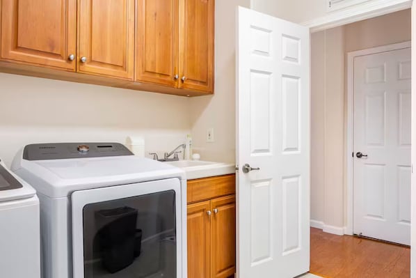 A laundry area with a washing machine, a dryer, wooden cabinets, a sink, and a white door.