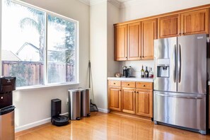 A kitchen with wooden cabinets, a stainless steel refrigerator, a window, and a trash can.