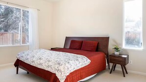A bedroom with a bed, a nightstand, a window, and a view of the outside.