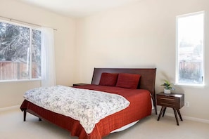 A bedroom with a bed, a nightstand, a window, and a view of the outside.