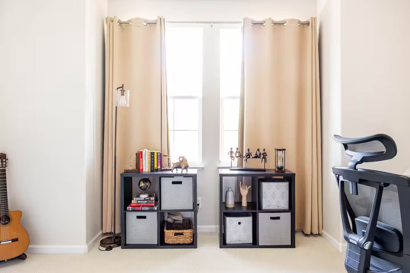 Una habitación con una puerta, una guitarra, dos estantes negros con diversos objetos y una silla negra.