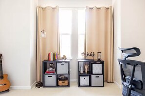A room with a door, a guitar, two black shelves with various items, and a black chair.