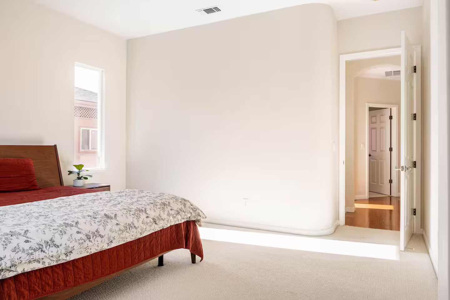 Un dormitorio con una cama, una mesita de noche, una ventana y una puerta que da a otra habitación.