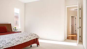 Un dormitorio con una cama, una mesita de noche, una ventana y una puerta que da a otra habitación.