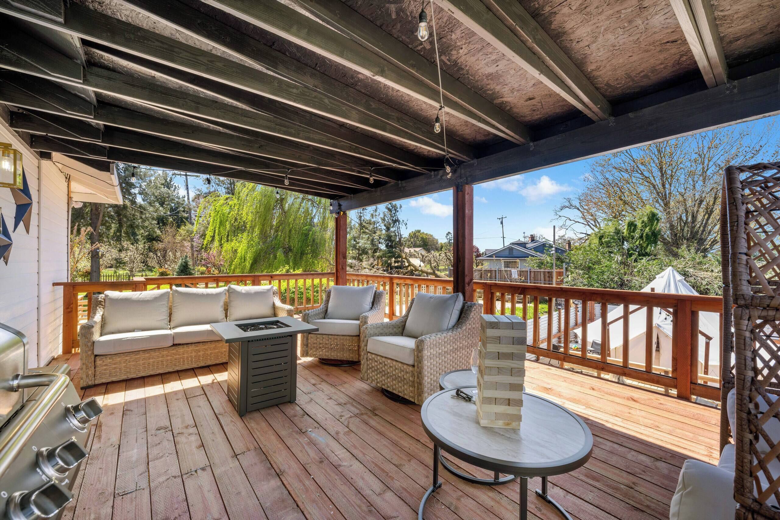 A covered outdoor deck with a grill, seating area, and a view of the surrounding landscape.