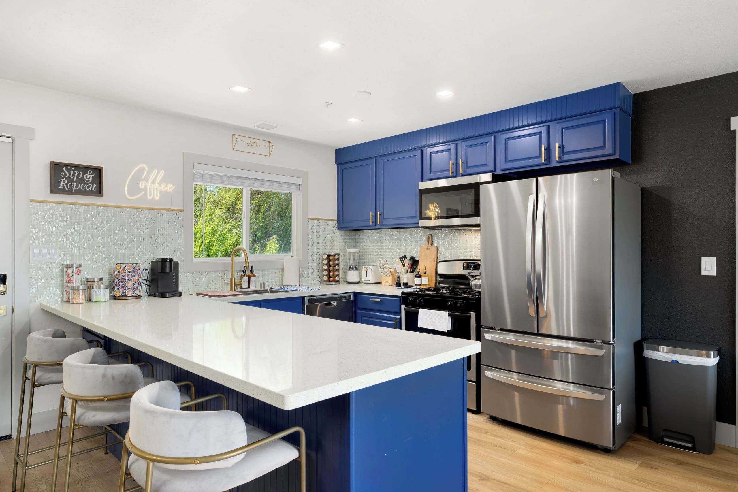 A modern kitchen with blue cabinets, a stainless steel refrigerator, and a white island with bar stools.