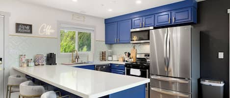 A modern kitchen with blue cabinets, a stainless steel refrigerator, and a white island with bar stools.