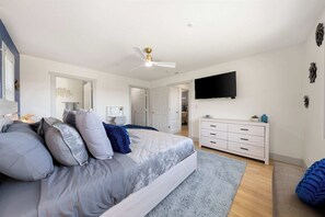 Ein modernes Schlafzimmer mit einem großen Bett, einem Deckenventilator, einem Flachbildfernseher und einer weißen Kommode.