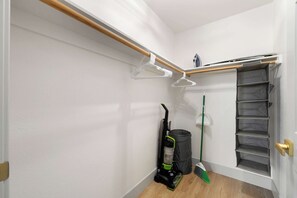 A corner of a room with a wooden beam, a white wall, a closet with a sliding door, a vacuum cleaner, a broom, and a trash bin. - Experience Serenity and Style in a Ryde Retreat. 8  Guests 2 bd 2ba, 3 Car Gar (Walnut Grove)
