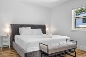 Un dormitorio moderno con una cama grande, mesitas de noche, un banco y una ventana con vistas.