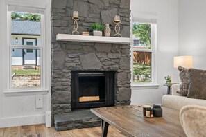 A room with a stone fireplace, a wooden table, and a couch. - Modern Getaway & Casita Near the Domain + Fire Pit Backyard, Sleeps 8 (Austin)