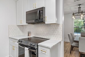 A modern kitchen with white cabinetry, a built-in microwave, a stovetop, and a dining area with a table and chairs. - Modern Getaway & Casita Near the Domain + Fire Pit Backyard, Sleeps 8 (Austin)