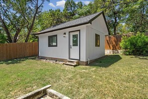 A small, single-story house with a white exterior, a dark roof, and a front door. - Modern Getaway & Casita Near the Domain + Fire Pit Backyard, Sleeps 8 (Austin)