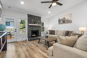 A living room with a fireplace, a sofa, a coffee table, and a ceiling fan. - Modern Getaway & Casita Near the Domain + Fire Pit Backyard, Sleeps 8 (Austin)