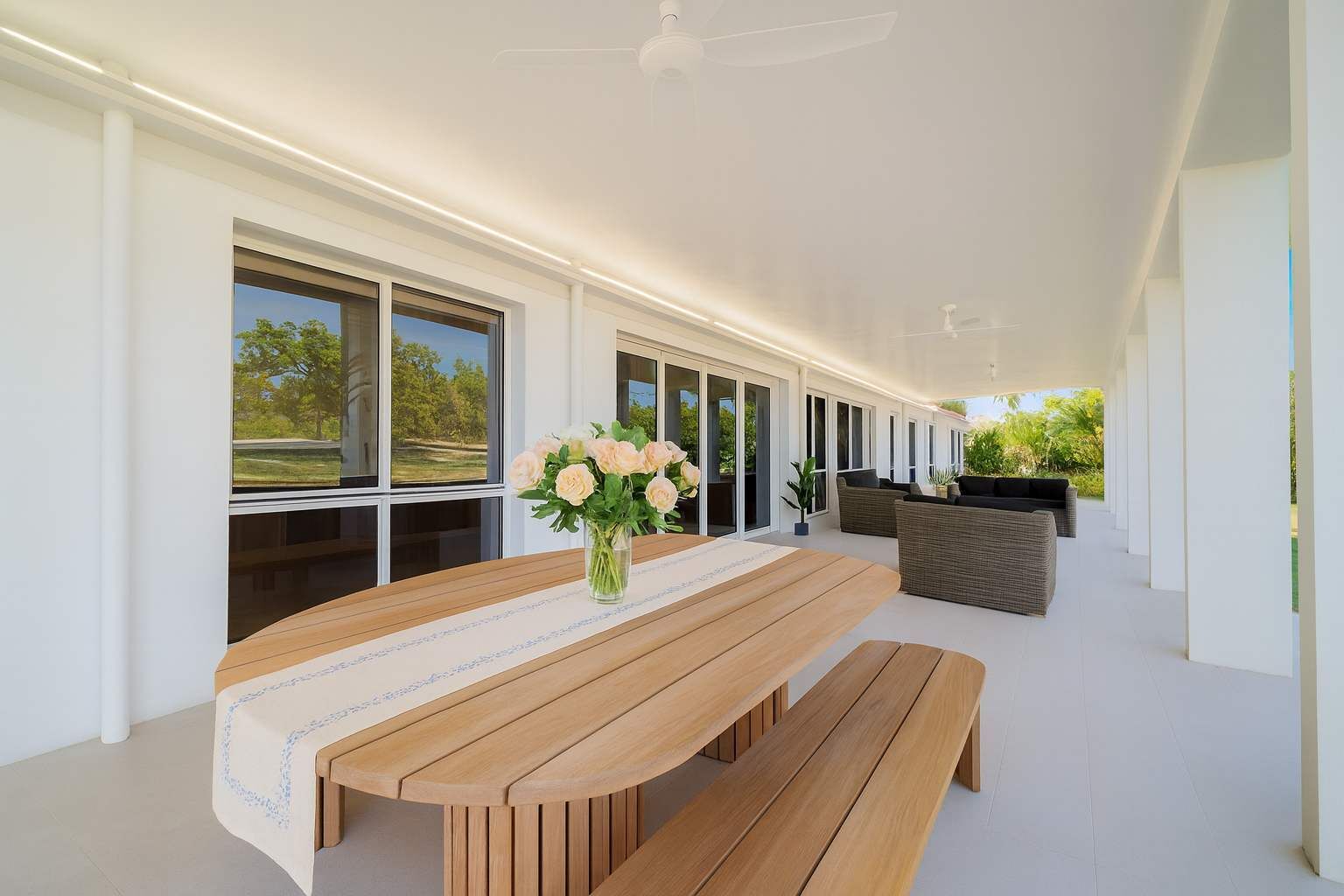 Un vaste espace extérieur aménagé pour les repas, avec une table et des bancs en bois, entouré de grandes fenêtres offrant une vue sur la verdure.