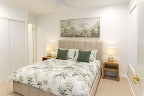Un dormitorio con cama, dos mesitas de noche con lámparas, ventilador de techo, puerta y un cuadro colgado en la pared.