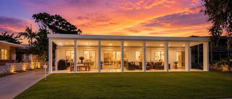 Une maison moderne dotée d’un patio couvert, d’une pelouse et offrant une vue sur un ciel au coucher du soleil.