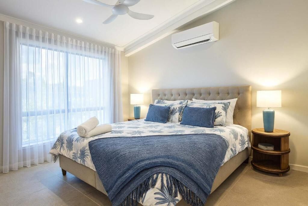 Une chambre à coucher comprenant un lit, deux lampes de chevet, un ventilateur de plafond et un appareil de climatisation.
