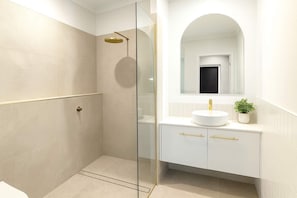 A modern bathroom with a glass-enclosed shower, a white sink with gold handles, and a mirror above the sink. - Beachfront Home Townsville (Pallarenda)