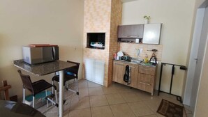 Uma cozinha compacta com micro-ondas, forno pequeno e pia. Possui uma área de refeições com mesa e cadeiras.
