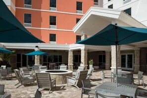 Eine Terrasse im Freien mit mehreren Sitzbereichen, darunter Stühle und Tische, und einer zentralen Feuerstelle.