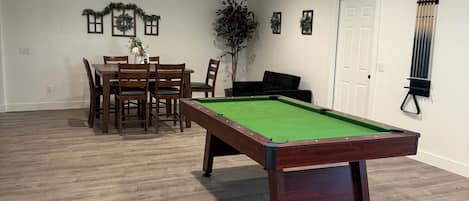 Ein Zimmer mit Billardtisch, Esstisch, Stühlen, einer Topfpflanze und einer Tür.