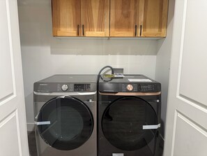 A laundry room with two front-loading washing machines and a dryer, wooden cabinets above, and a white door frame. - Come enjoy this 3 bedroom basement apartment in the great city of Honeyville. (Brigham City)