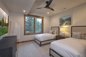 A bedroom with two beds, a ceiling fan, a window with a view of trees, and a painting on the wall. - Parkside Teton Springs Cabin in Victor, ID w/ A/C & Hot Tub (Victor)