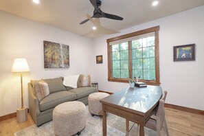 A living room with a sofa, ottomans, a table, a lamp, and artwork on the walls. - Parkside Teton Springs Cabin in Victor, ID w/ A/C & Hot Tub (Victor)