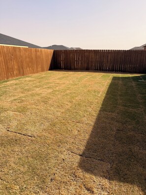 A fenced backyard with a grassy area and a wooden fence. - 3-bedroom house in lovely Lubbock with AC for your stay (Lubbock)