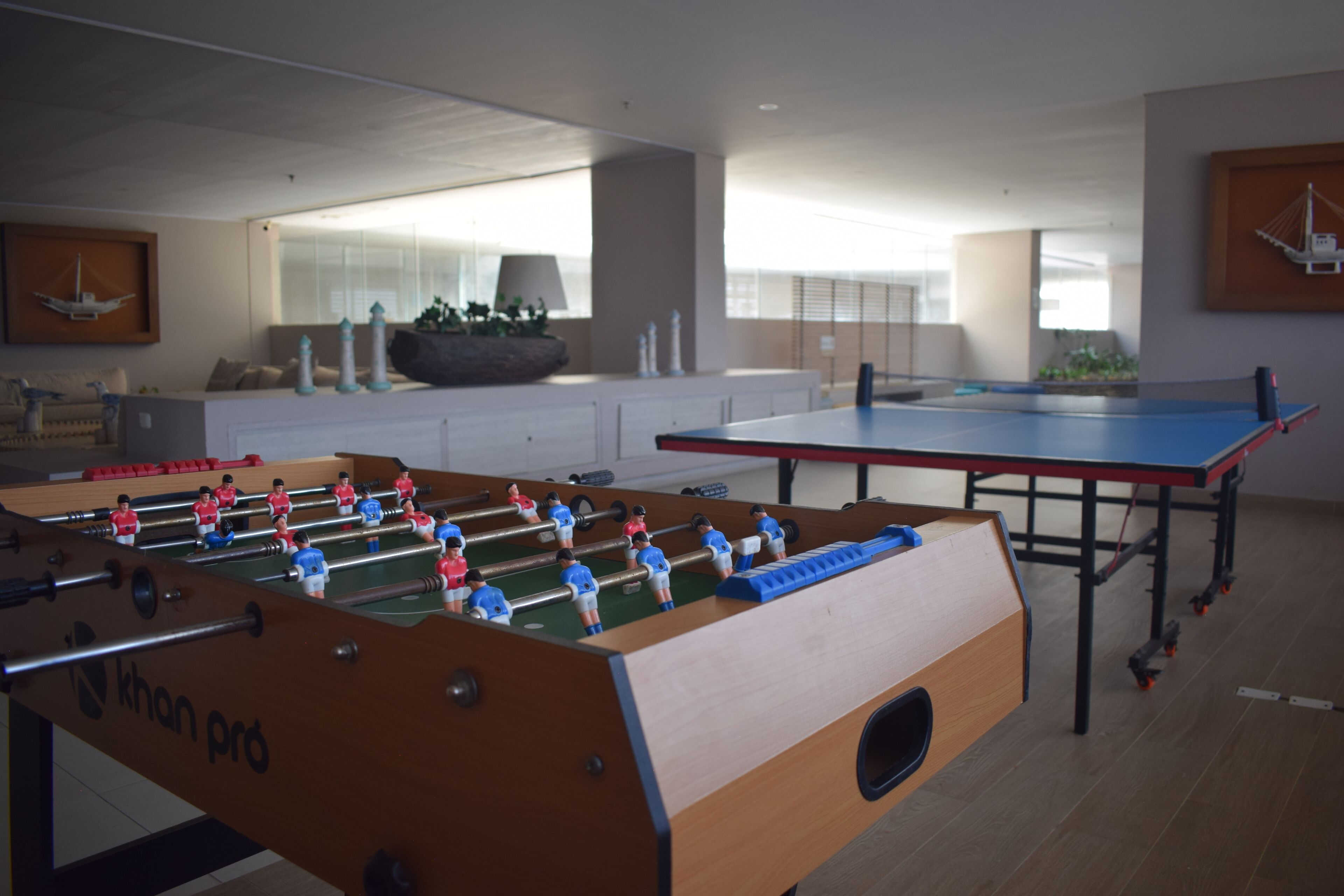 Ein Fußballtisch in einem Raum mit einem Tischtennis-Tisch, Holzboden und einem großen Fenster.