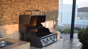 An outdoor kitchen with a stone wall backdrop, a gas stove, and a grill. - Santa Marta: Sunset View, Pools, and Private Beach in Pozos Colorados (Santa Marta)