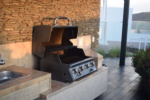 Eine Außenküche mit einer Wand aus Stein, einem Gasherd und einem Grill.