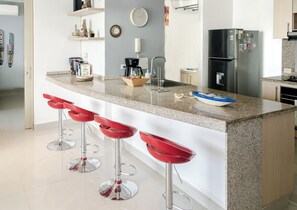 A modern kitchen with a granite countertop, stainless steel appliances, and red bar stools. - Santa Marta: Sunset View, Pools, and Private Beach in Pozos Colorados (Santa Marta)
