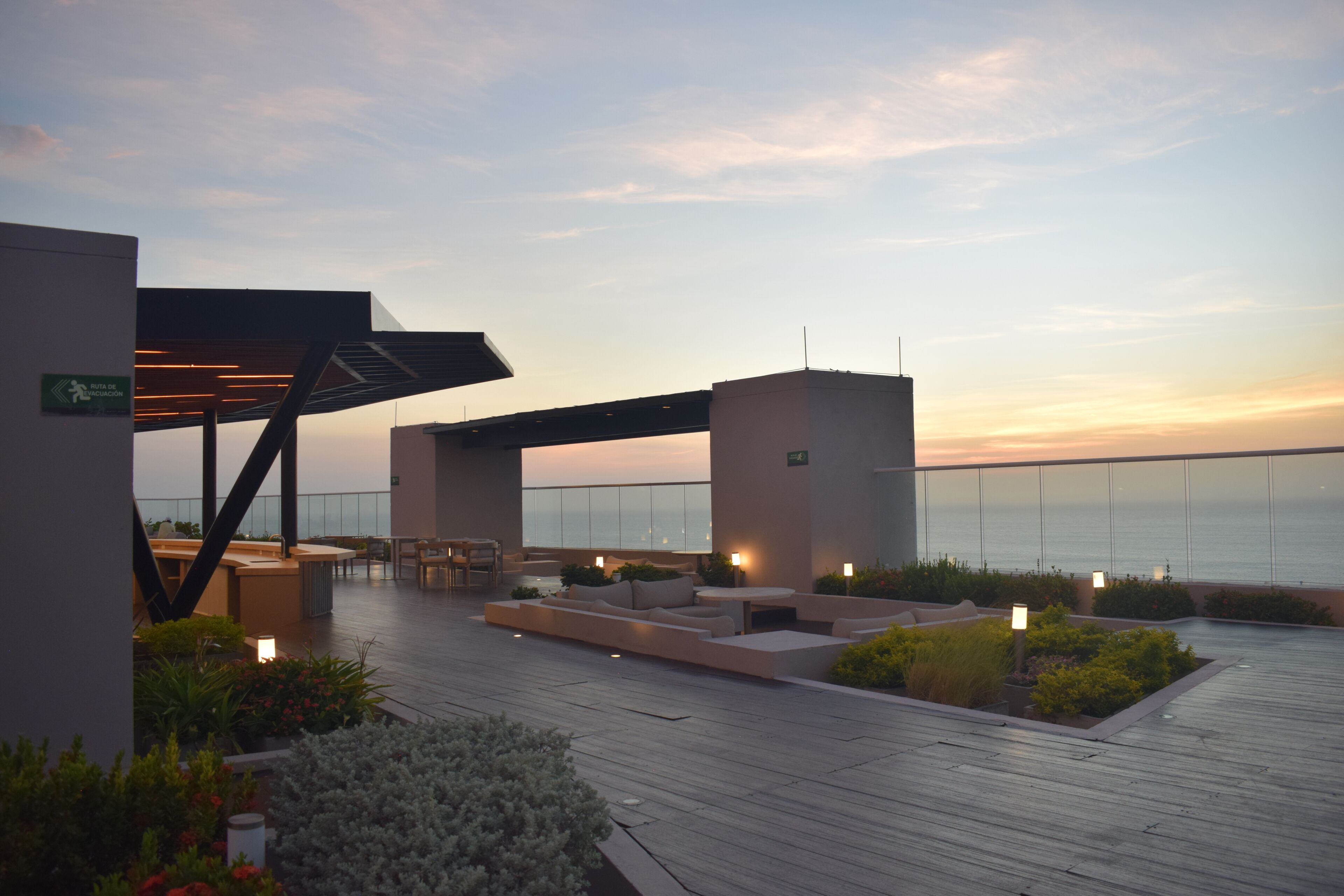 An outdoor terrace with seating, a view of the sea, and a building with an evacuation route sign.