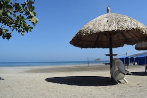 Ein Strand mit einem reetgedeckten Sonnenschirm, einem Volleyballnetz und einem klaren, blauen Himmel.