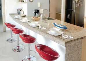 A kitchen with a granite countertop, stainless steel appliances, and red bar stools. - Santa Marta: Sunset View, Pools, and Private Beach in Pozos Colorados (Santa Marta)